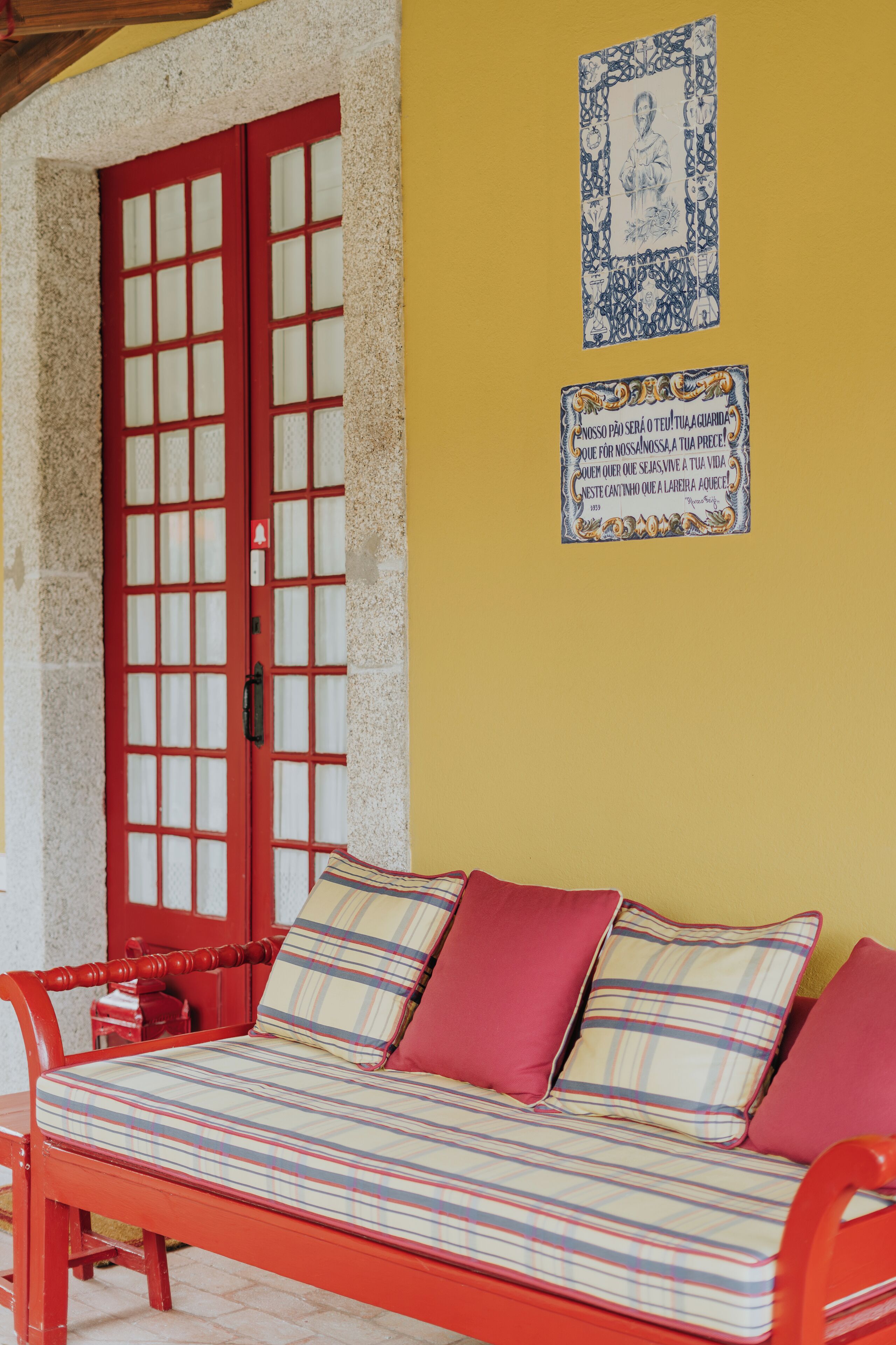 A room with a red door, a bench with striped cushions, and two framed pictures on the wall.