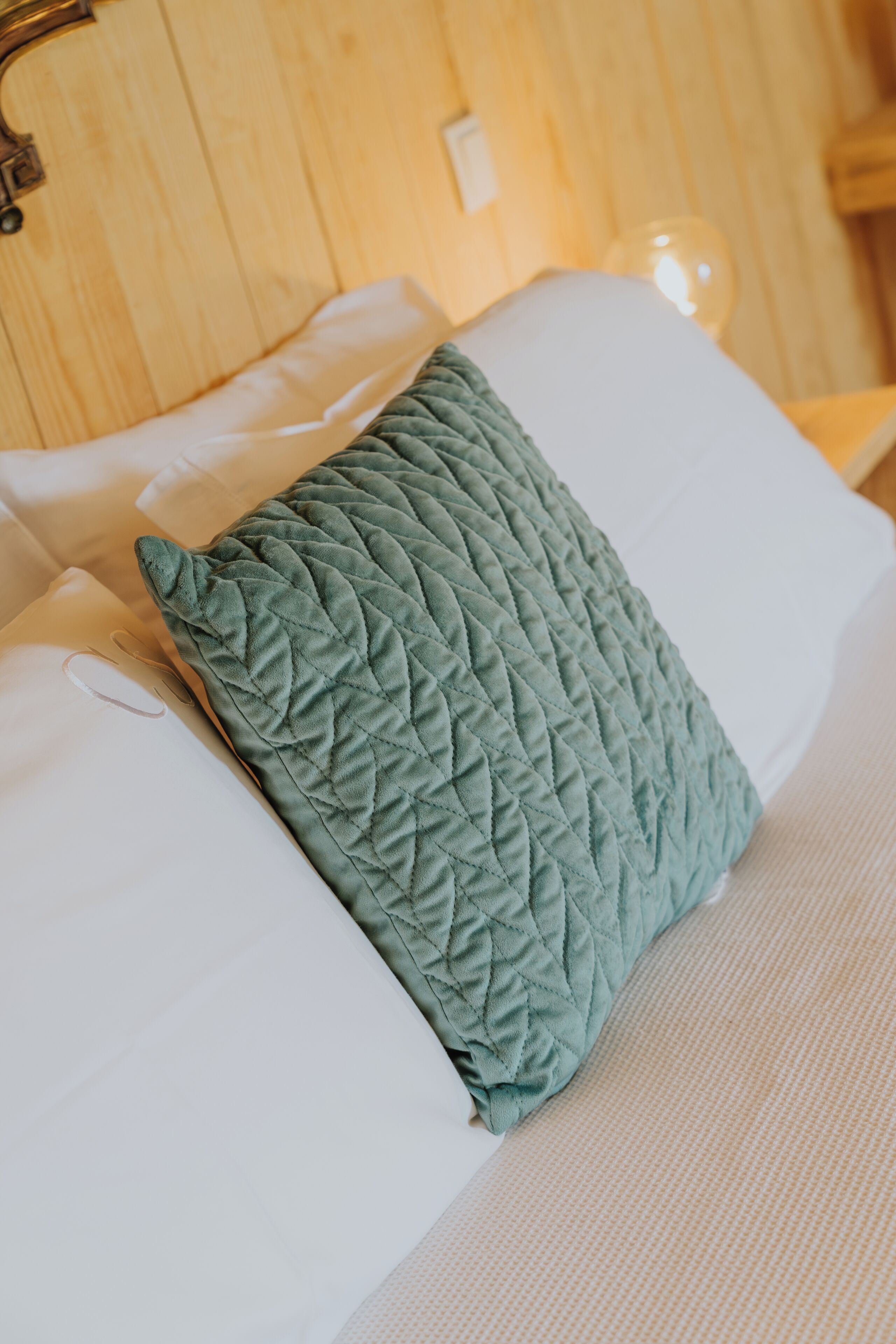 A bed with a quilted green pillow and white sheets.
