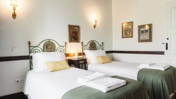 A hotel room with two beds, green bedspreads, white linens, and wall-mounted lamps.