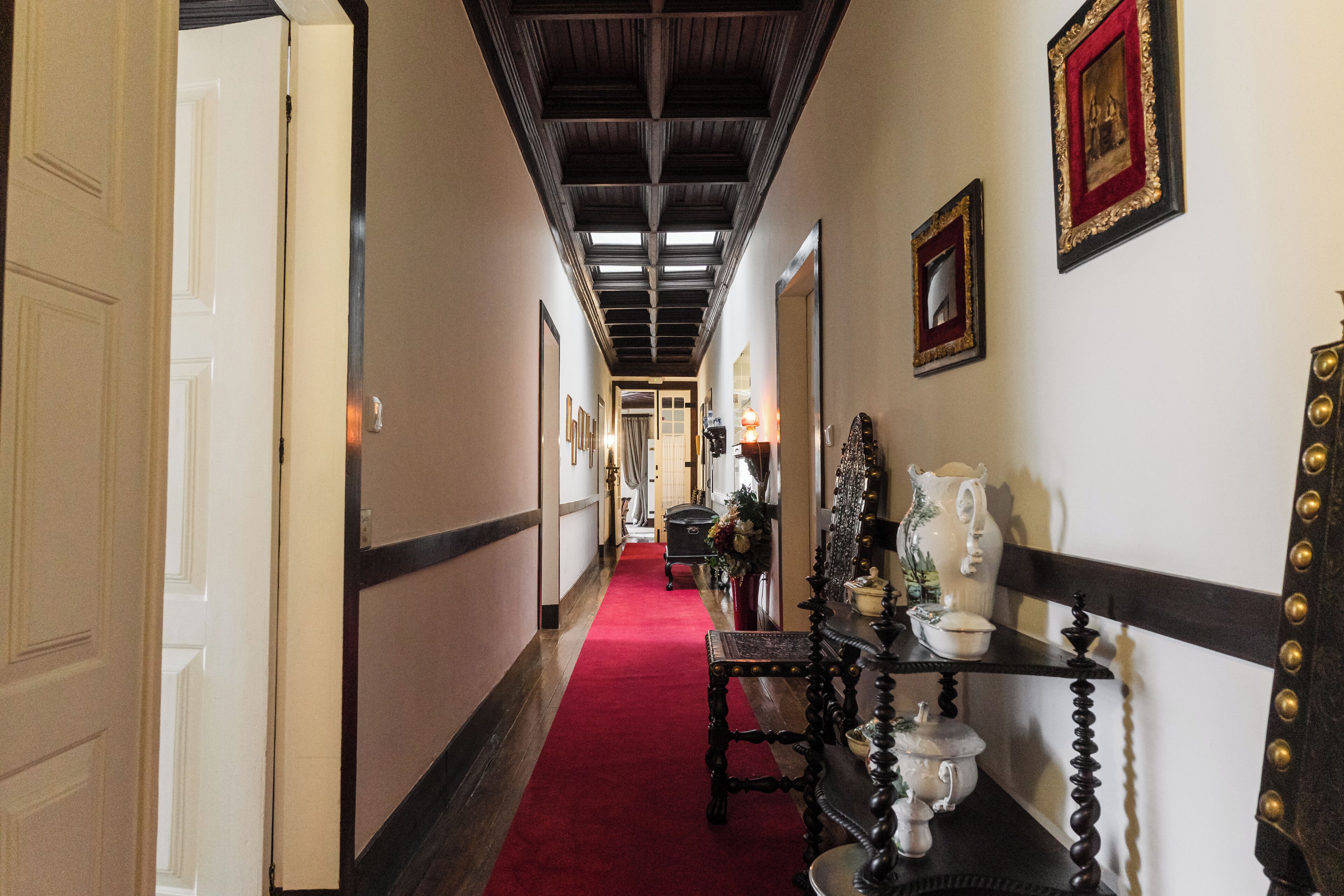 A hallway with a red carpet, wooden ceiling beams, and a wall-mounted display of white ceramic items.