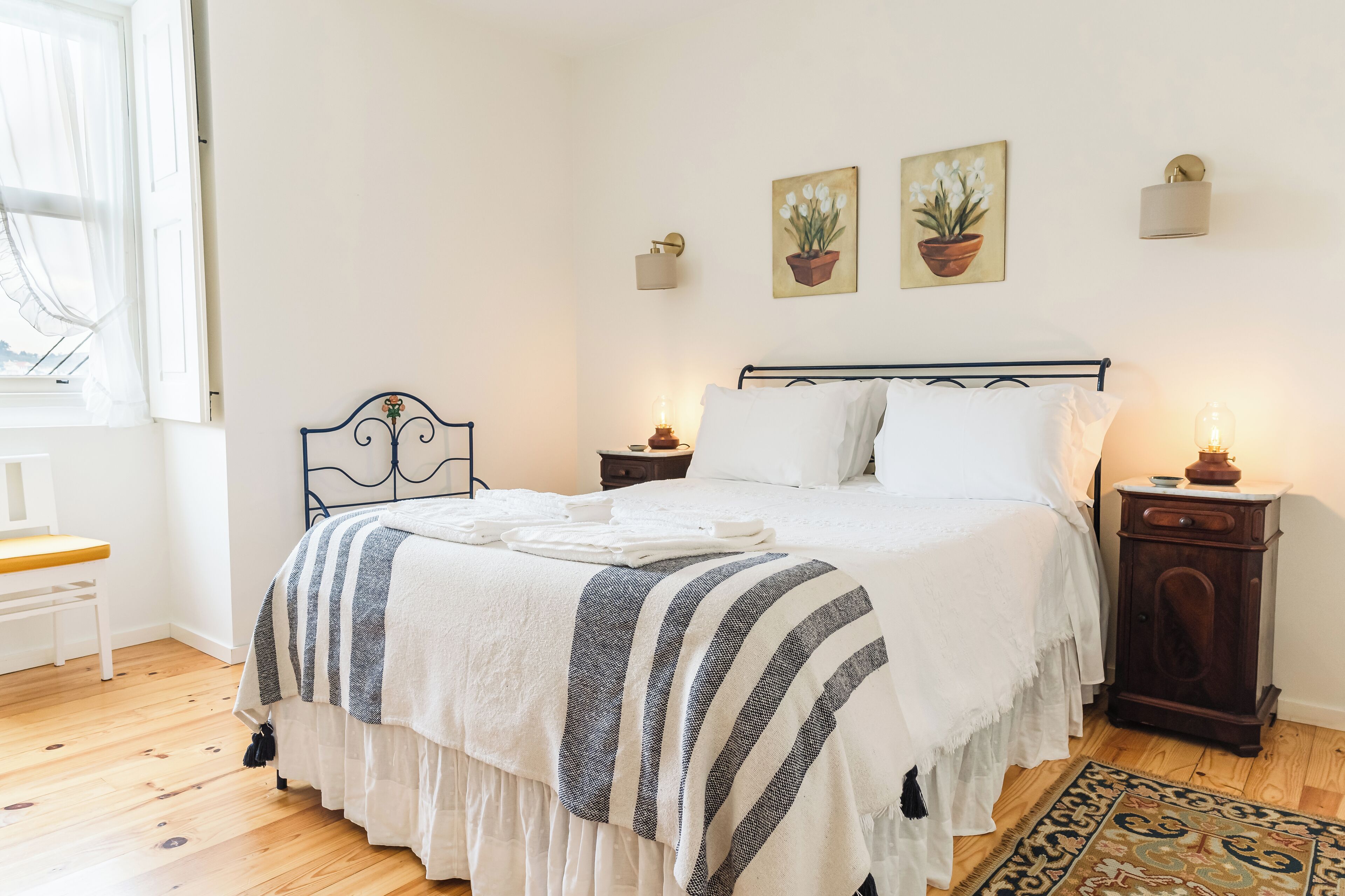 A neatly arranged bedroom with a bed, bedside tables, a chair, and artwork on the wall.