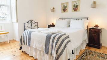 A neatly arranged bedroom with a bed, bedside tables, a chair, and artwork on the wall.