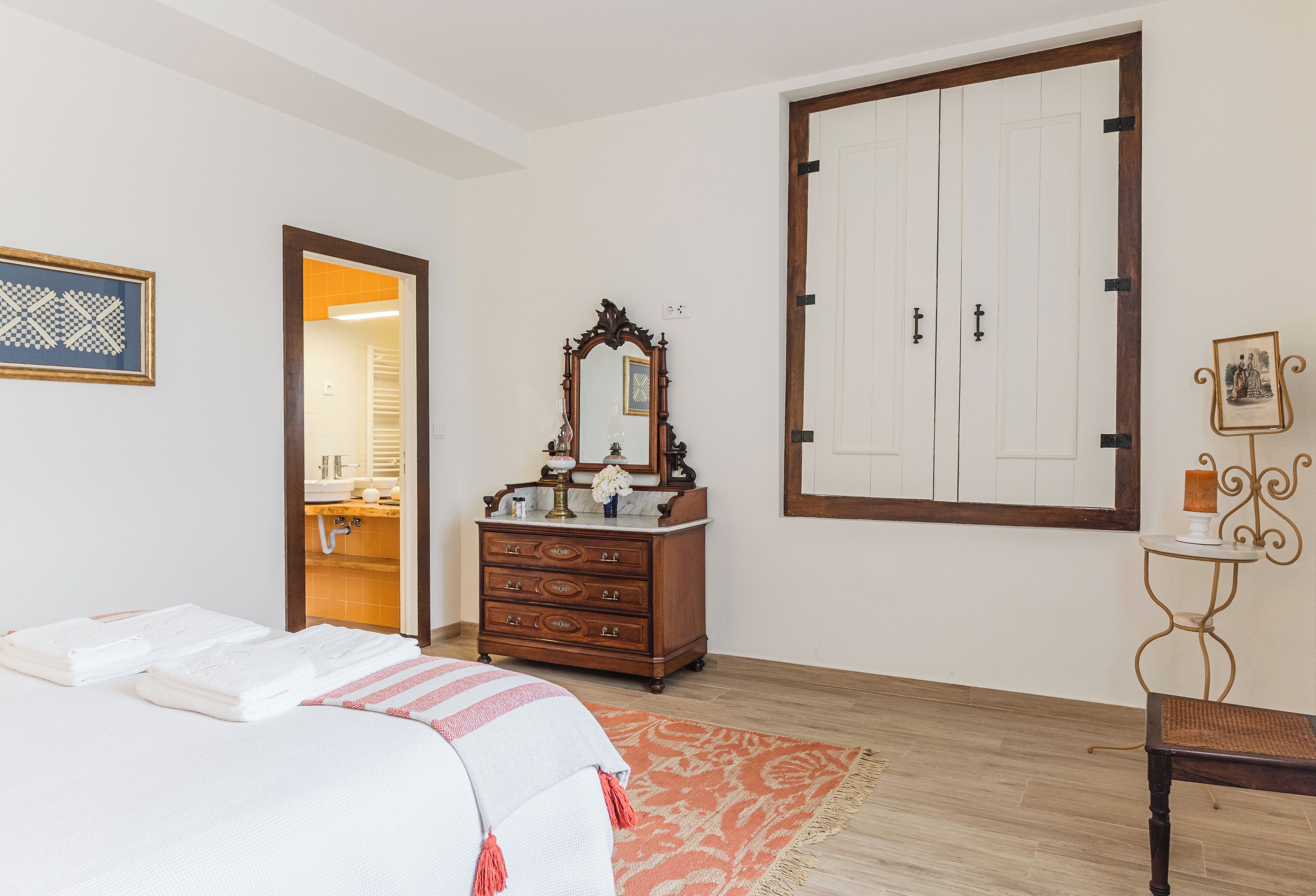 A bedroom with a bed, a dresser, a mirror, a wardrobe, and a small table with a chair.