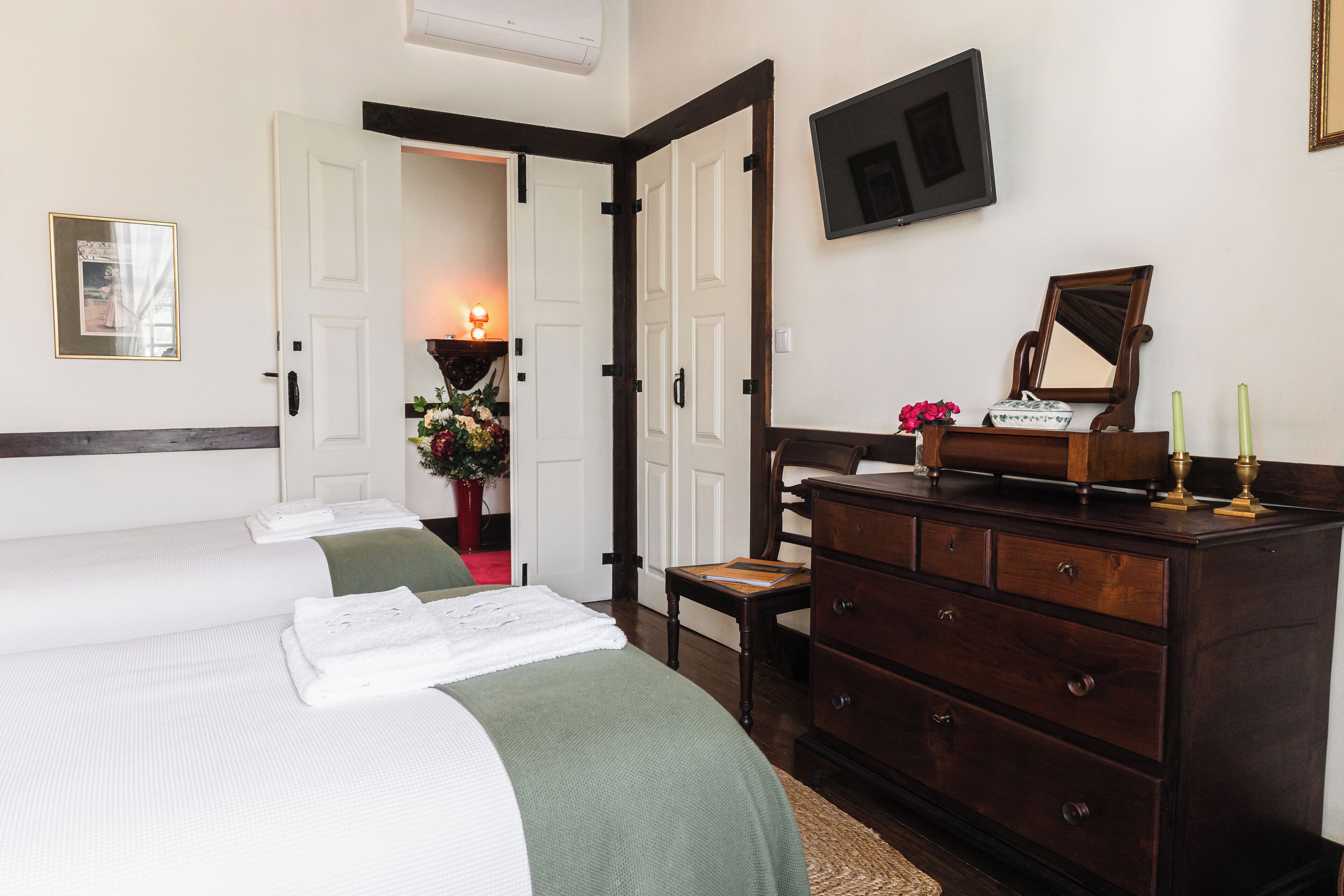 Une chambre d’hôtel avec deux lits, une commode, un miroir et un téléviseur fixé au mur.
