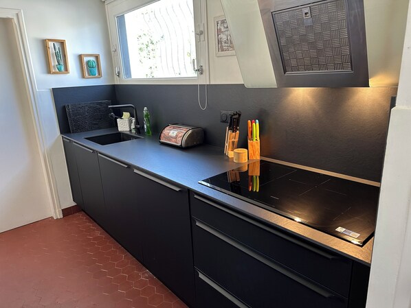 A modern kitchen with a black countertop, stainless steel appliances, and a window with a view of trees. - Beautiful property, very good location (Le Touquet)