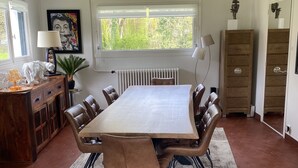 Un comedor con una mesa grande, seis sillas, un radiador, un ventanal con vistas a la vegetación, un armario y una lámpara.