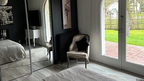 Un dormitorio con un espejo grande, una silla, una cama y vistas al exterior a través de una puerta de vidrio.