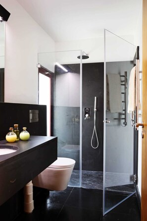 A modern bathroom with a glass-enclosed shower, a dark marble countertop, and a pink toilet.
