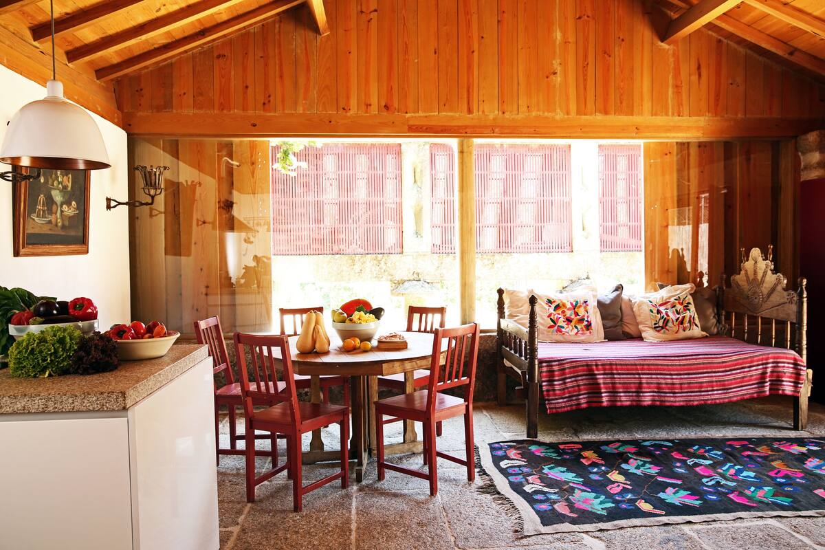 Ein gemütliches Zimmer mit Holzbalkendecke, einem Esstisch mit Stühlen, einem Bett mit Decke und einem Fenster mit Fensterläden.