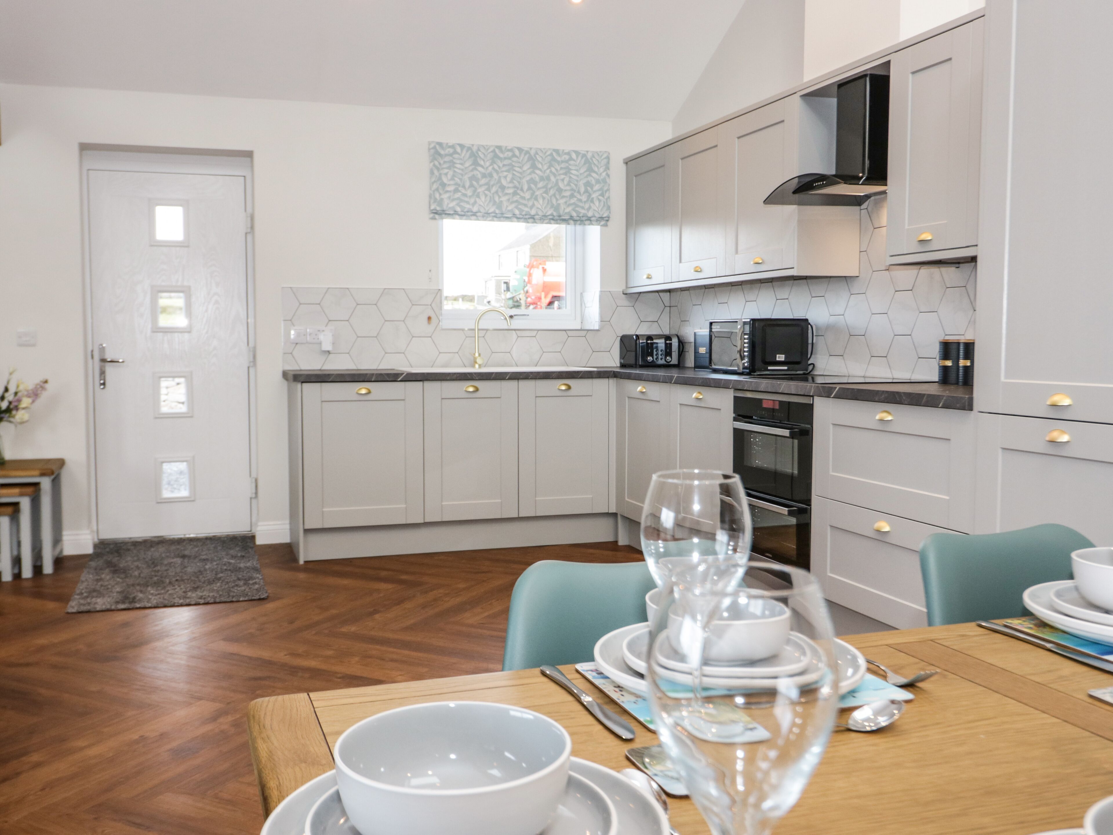 A modern kitchen with grey cabinets, a microwave, and a window with patterned curtains.