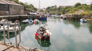 Un port de plaisance avec des bateaux amarrés, un bâtiment en pierre et, au fond, une colline verdoyante.