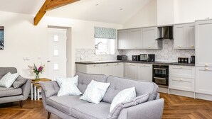 Une cuisine moderne avec des meubles blancs, une cuisinière noire et un four à micro-ondes. Le salon est doté d’un canapé gris agrémenté de coussins à motifs.