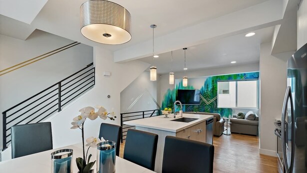 Una cocina moderna con una isla central, un comedor con sillas y una escalera.