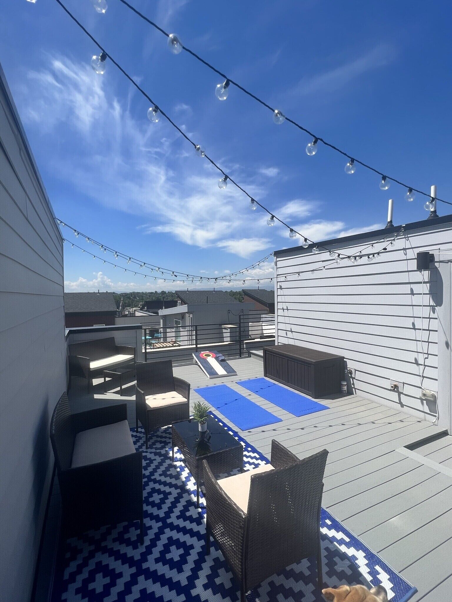 A rooftop deck with outdoor furniture, string lights, and a blue patterned mat.