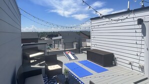 Terraza en la azotea con mobiliario exterior, luces colgantes y un tapete azul estampado.