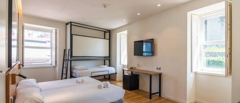 A hotel room with a bunk bed, a desk, a television, and a window with a view of the outside.