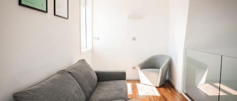 A modern living room with a grey sofa, a glass partition, and a wooden floor.