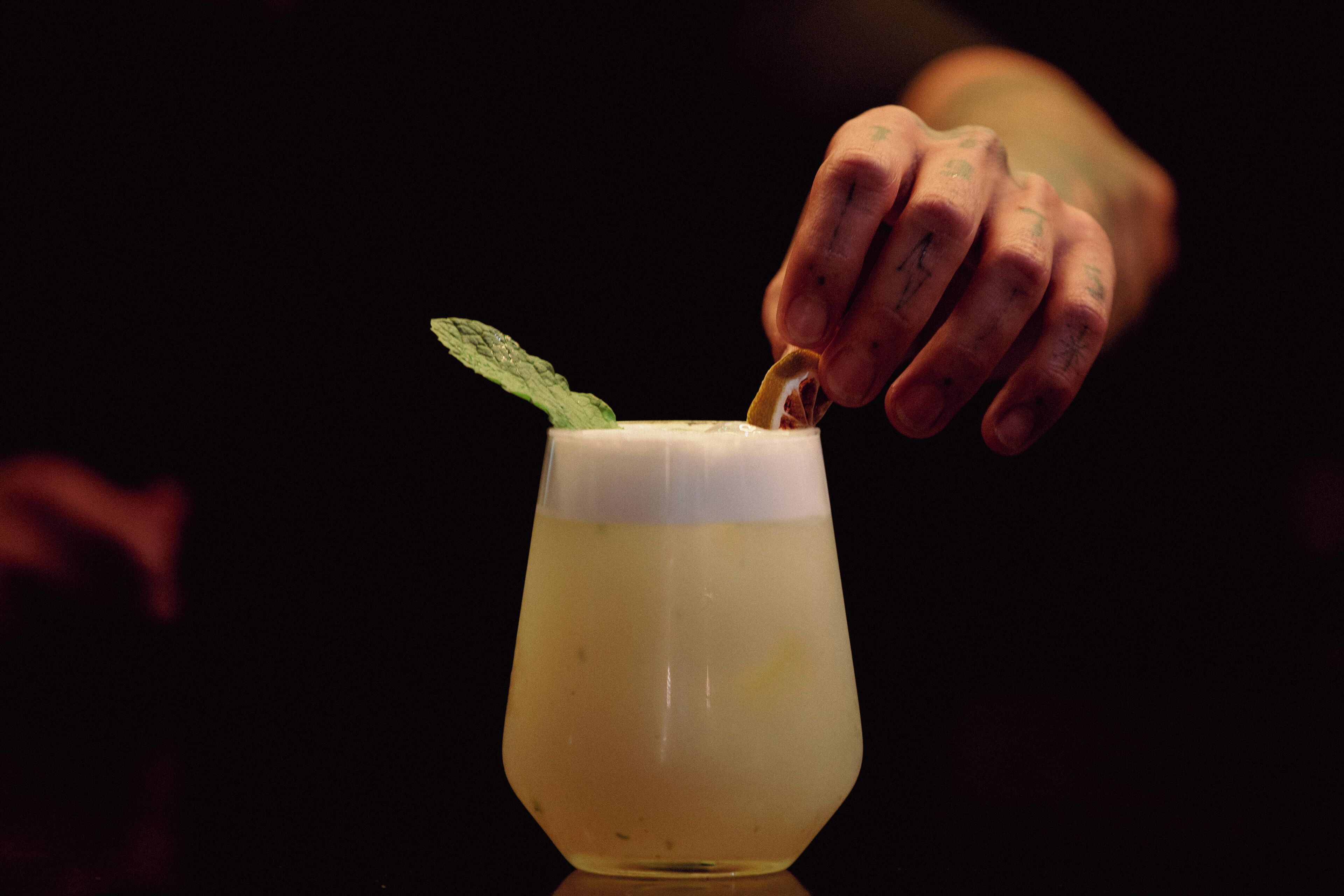 Una mano che depone una fetta di limone in un bicchiere guarnito con foglie di menta.