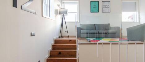 A staircase leading to a living area with a grey sofa, a floor lamp, and wall art.