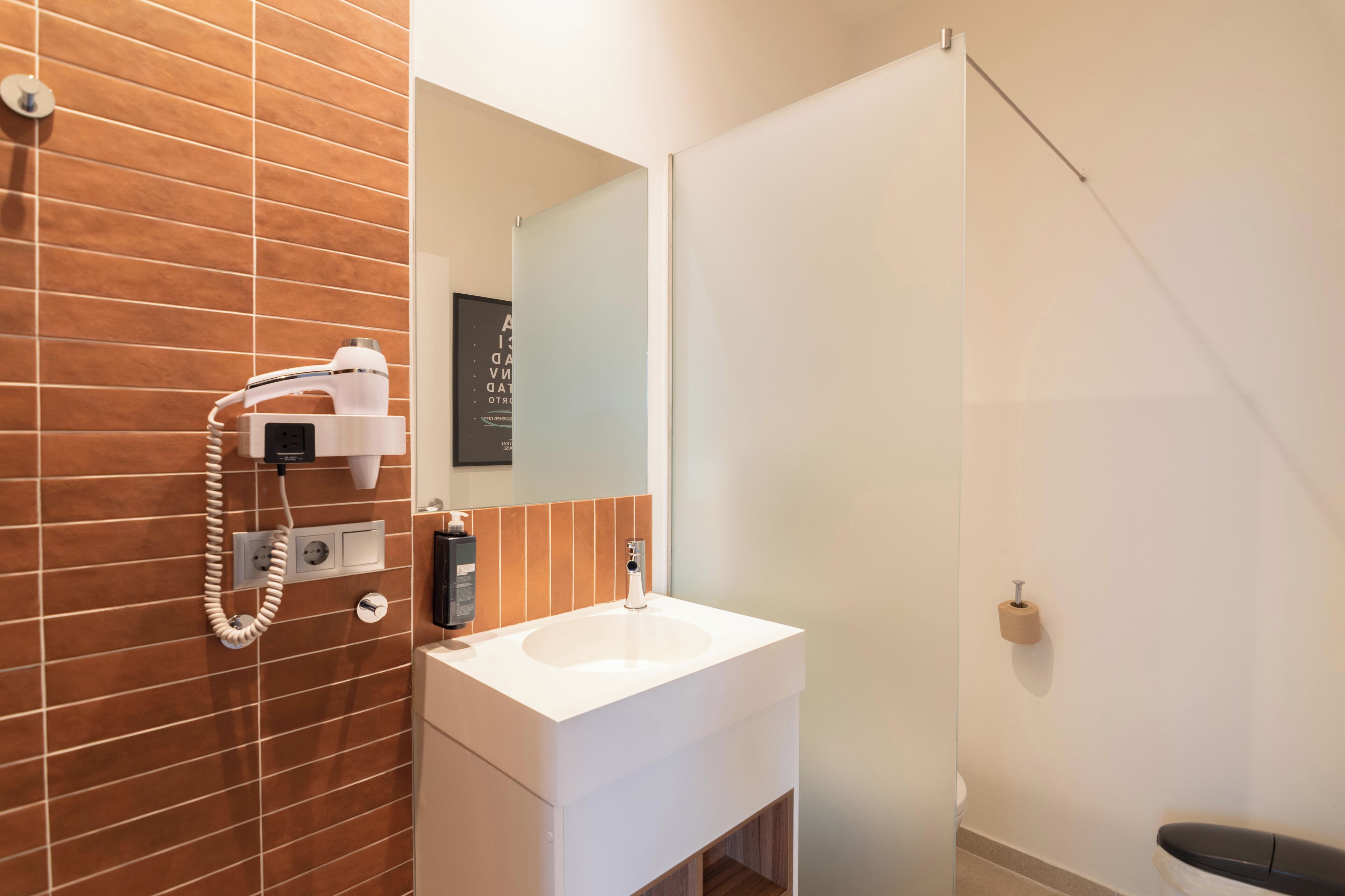 Une salle de bain avec un lavabo blanc, un sèche-cheveux et un miroir.