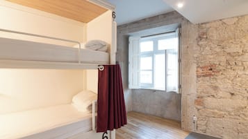 Quarto com beliches, parede de pedra, janela com persianas e piso de madeira.