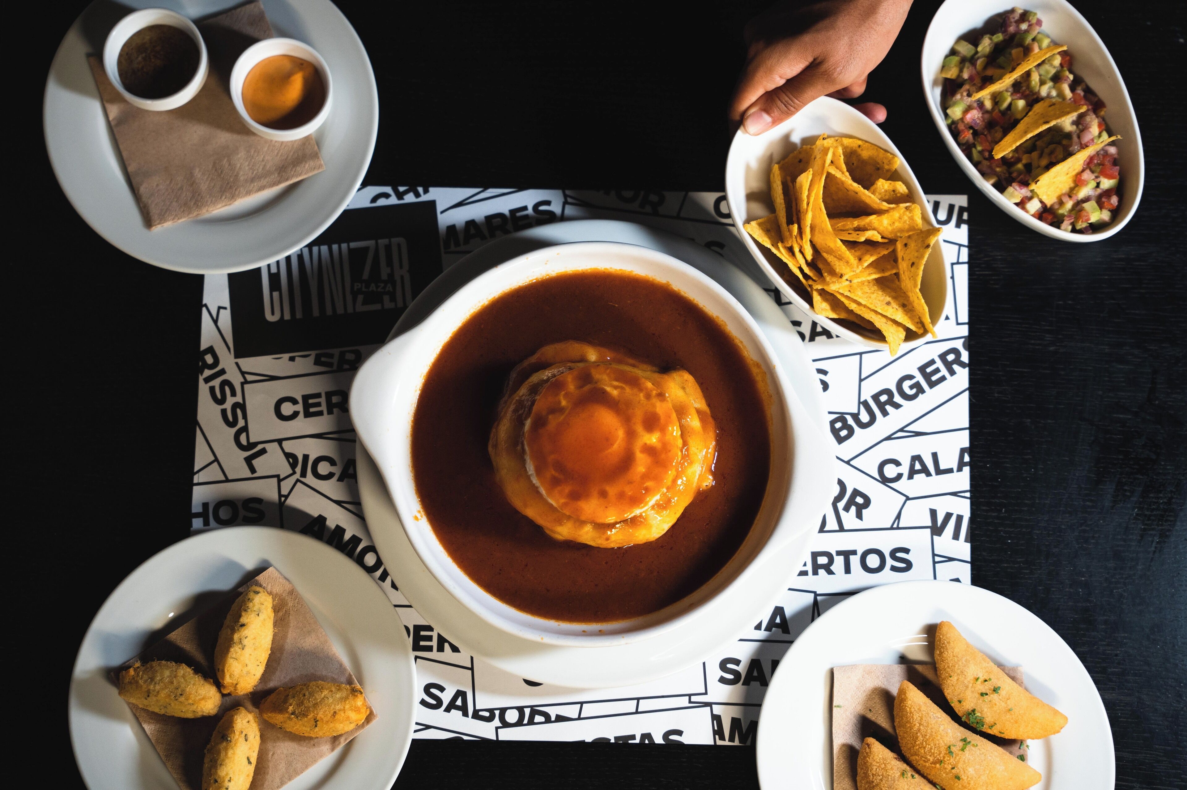 Una mesa con diversos platos, incluyendo un tazón de sopa, un plato de papas fritas y un tazón de salsa.
