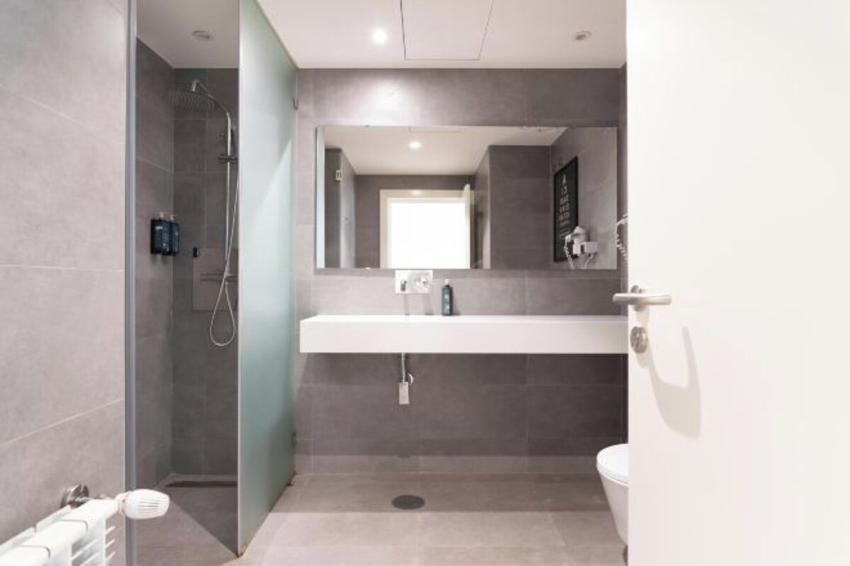 A modern bathroom with a walk-in shower, a large mirror, and a white sink.