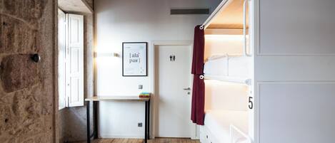 Una habitación con pared de piedra, suelo de madera, una puerta blanca, un cuadro enmarcado en la pared y un armario blanco con cajones.
