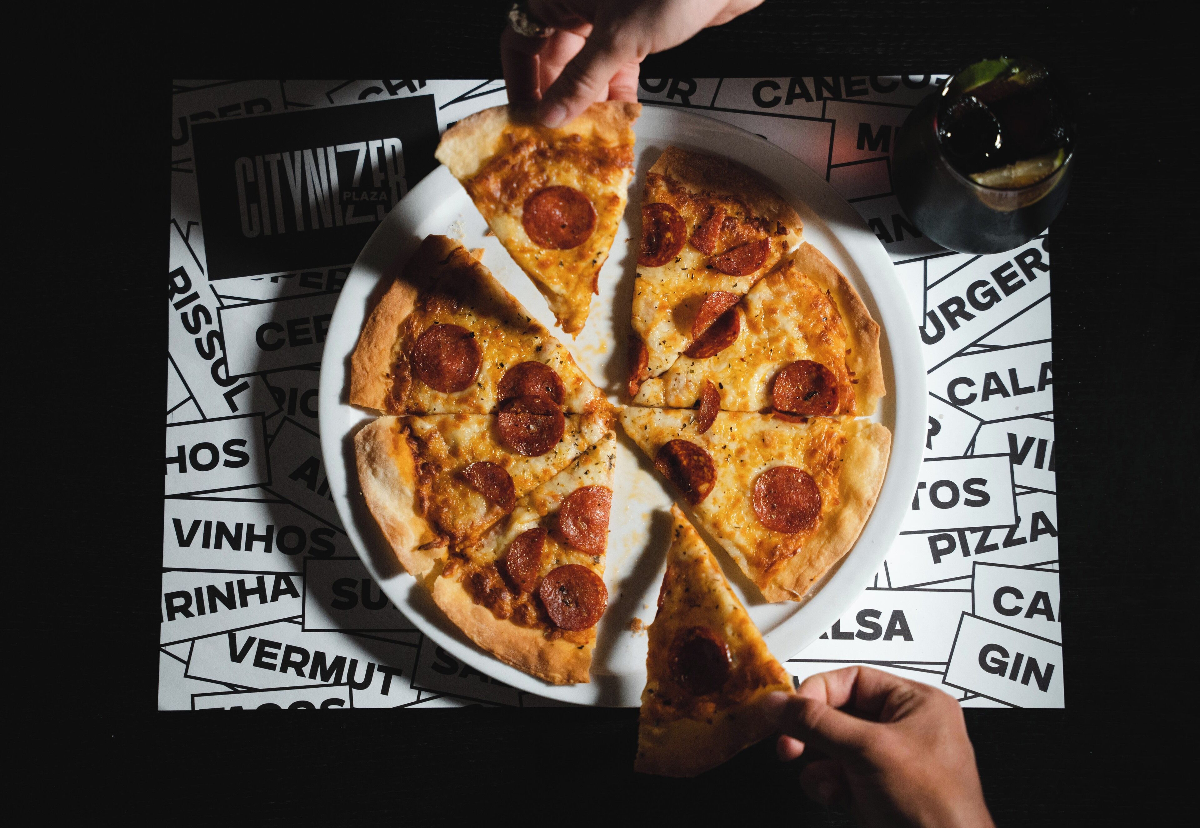 Pizza con rodajas de pepperoni sobre un plato blanco, colocada sobre una superficie negra con texto impreso.