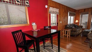 A dining area with a red wall, wooden flooring, a table with chairs, and a sofa. - Close to Town • Mountain Views • Fast Wifi • Pet Friendly (Murphy)