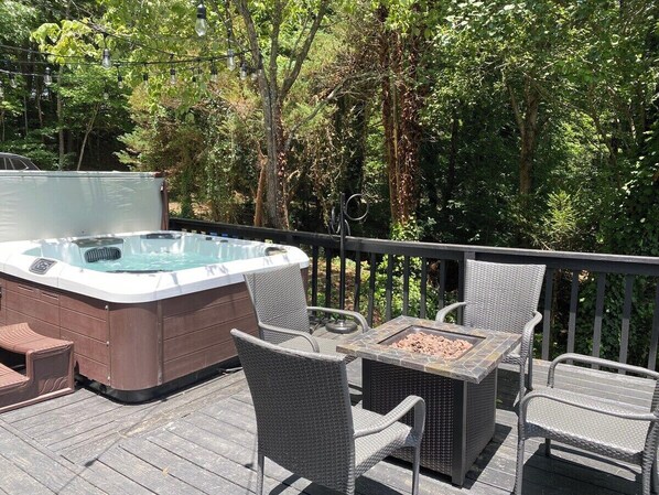 A hot tub on a wooden deck with wicker chairs and a table.