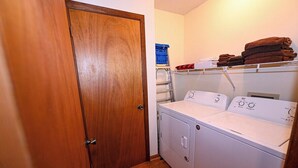 A laundry room with a white washer and dryer, a wooden door, and a shelf with folded towels. - Close to Town • Mountain Views • Fast Wifi • Pet Friendly (Murphy)