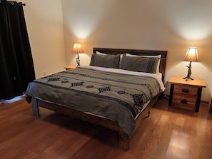 Een bed met een beddegoed met patroon, twee bedlampjes en een nachtkastje van hout met een lade.
