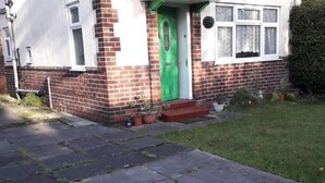 Una casa de ladrillo de dos pisos con una puerta verde, un pequeño porche y plantas en macetas.