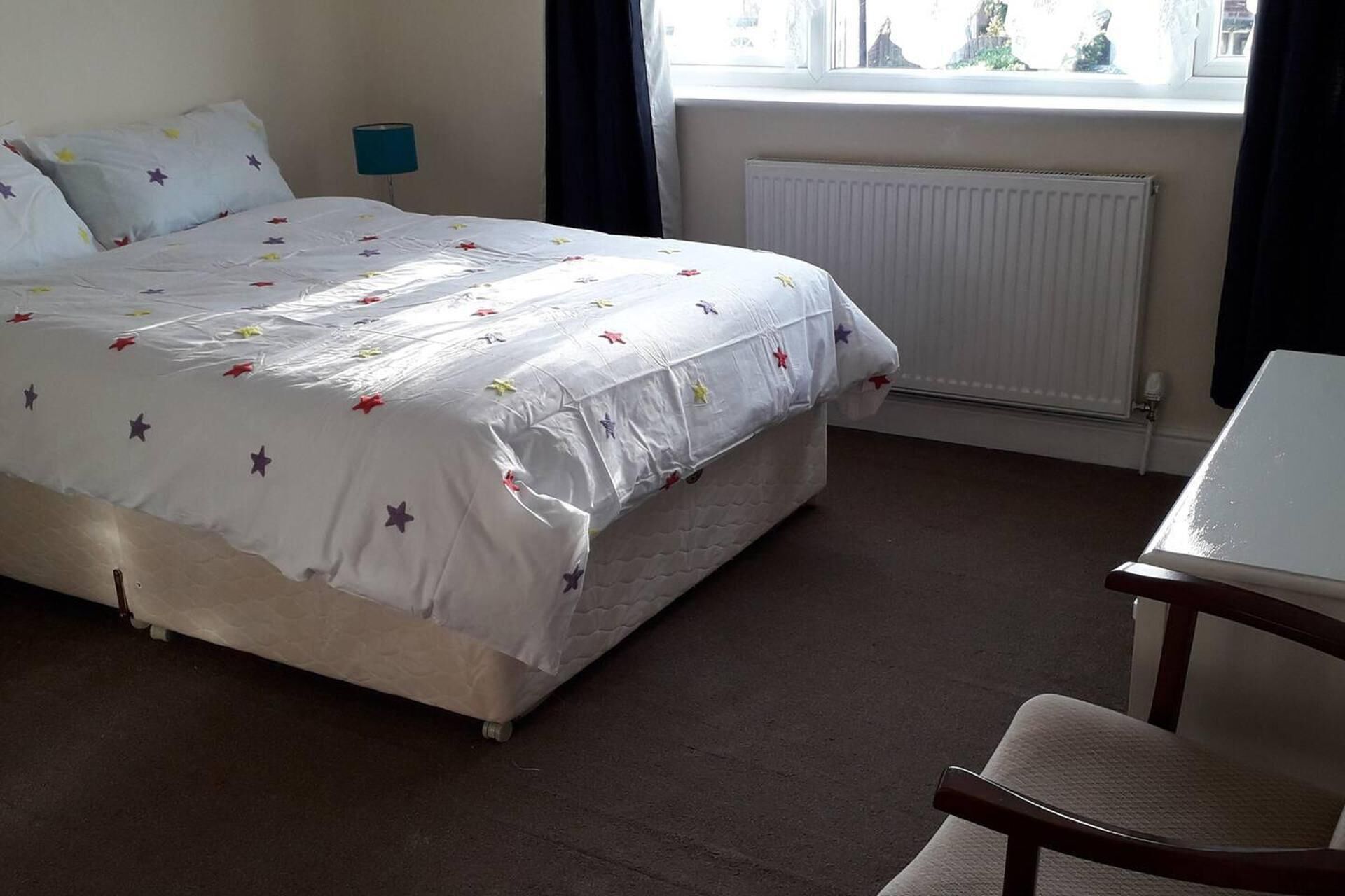Una habitación de hotel con cama, una silla, una mesita de noche, una ventana con cortinas y un radiador.