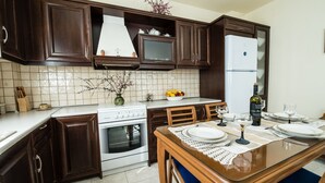 Une cuisine avec des meubles de rangement en bois foncé, un réfrigérateur blanc, une cuisinière et une table à manger dressée avec des assiettes et des verres.