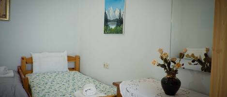 Une chambre à coucher avec un lit en bois, une petite table sur laquelle est posé un vase de fleurs, et un tableau représentant un paysage de montagne accroché au mur.