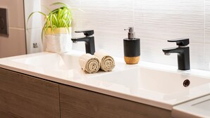 Un baño moderno con un lavamanos blanco, grifos negros y una planta en maceta.
