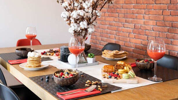 Una mesa de comedor con diversos alimentos y bebidas, incluyendo un tazón de cereal, pasteles y un vaso de bebida roja.