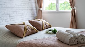 Una cama bien hecha con dos almohadas, una toalla enrollada y un pequeño ramo de flores.