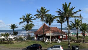 A beachside restaurant with outdoor seating, palm trees, and a view of the ocean. - Beachfront House (SP)