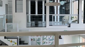 A modern interior with a staircase, a dining area with chairs, and a large window. - Beachfront House (SP)