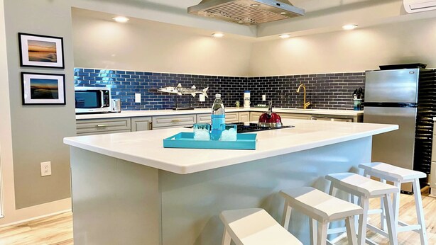 A modern kitchen with a central island, white bar stools, a stainless steel refrigerator, and a blue backsplash. - Channel View Residence at the Dygert House (Clayton)