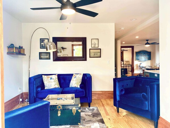 Un salon avec un canapé bleu, un fauteuil assorti, une table basse en bois et une valise ancienne.