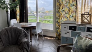 A room with a dining table, chairs, a sofa, a cabinet with drawers, and a large window with curtains. - T.2 SUPERB SEA VIEW "COCOONING FAVORITE" CLASS 2 STARS!!!! (La Grande-Motte)