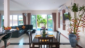 A spacious living area with a sofa, dining table, and chairs, a large window with a view of greenery, and a potted plant. - K-Bunk Villa Ao Nang (Krabi)