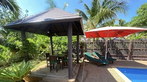 A covered patio area with a table and chairs, a pool, and lounge chairs. - K-Bunk Villa Ao Nang (Krabi)