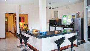 A modern kitchen with a central island, bar stools, a refrigerator, and a ceiling fan. - K-Bunk Villa Ao Nang (Krabi)