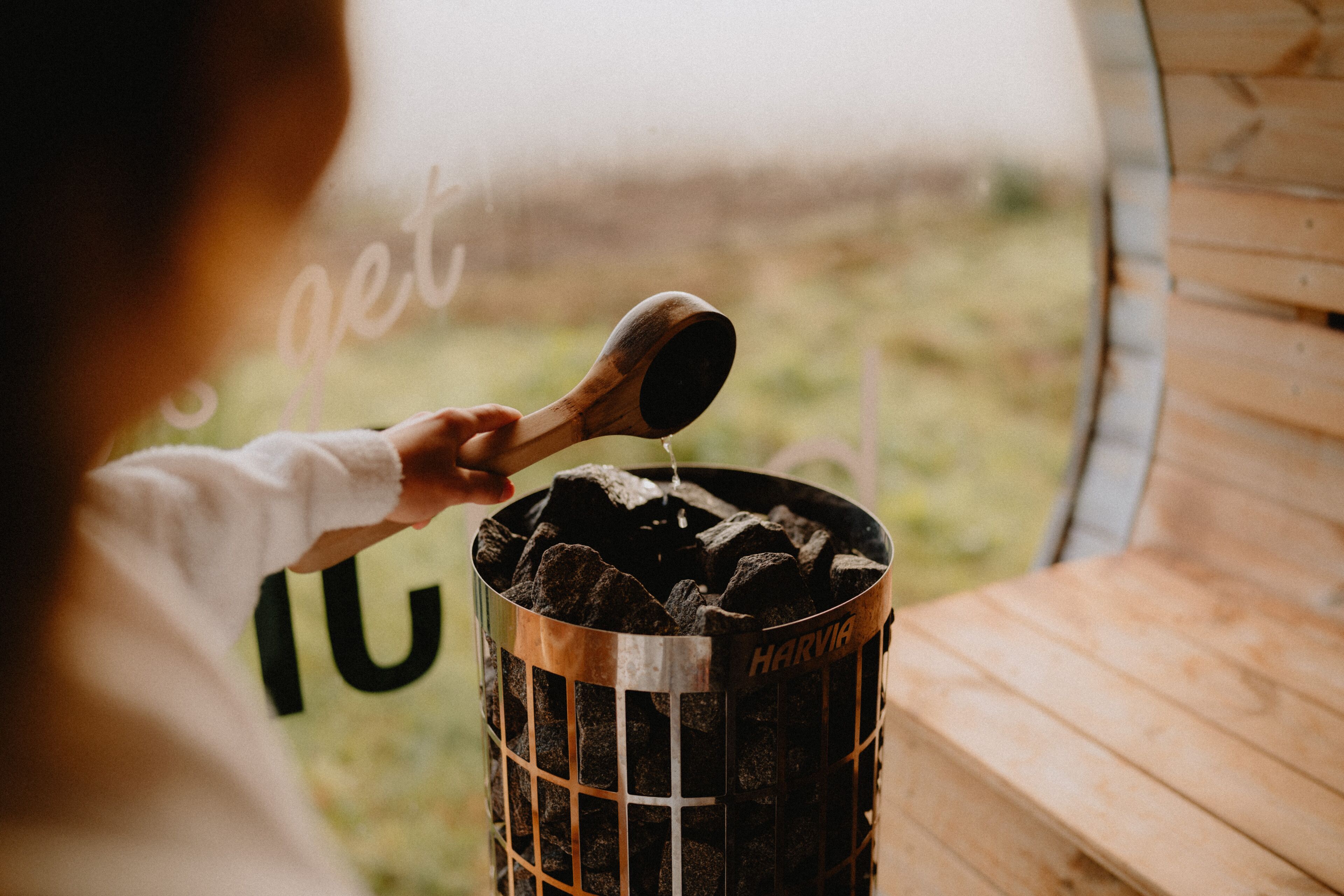 A person pouring water into a charcoal grill labeled "HARVIA".