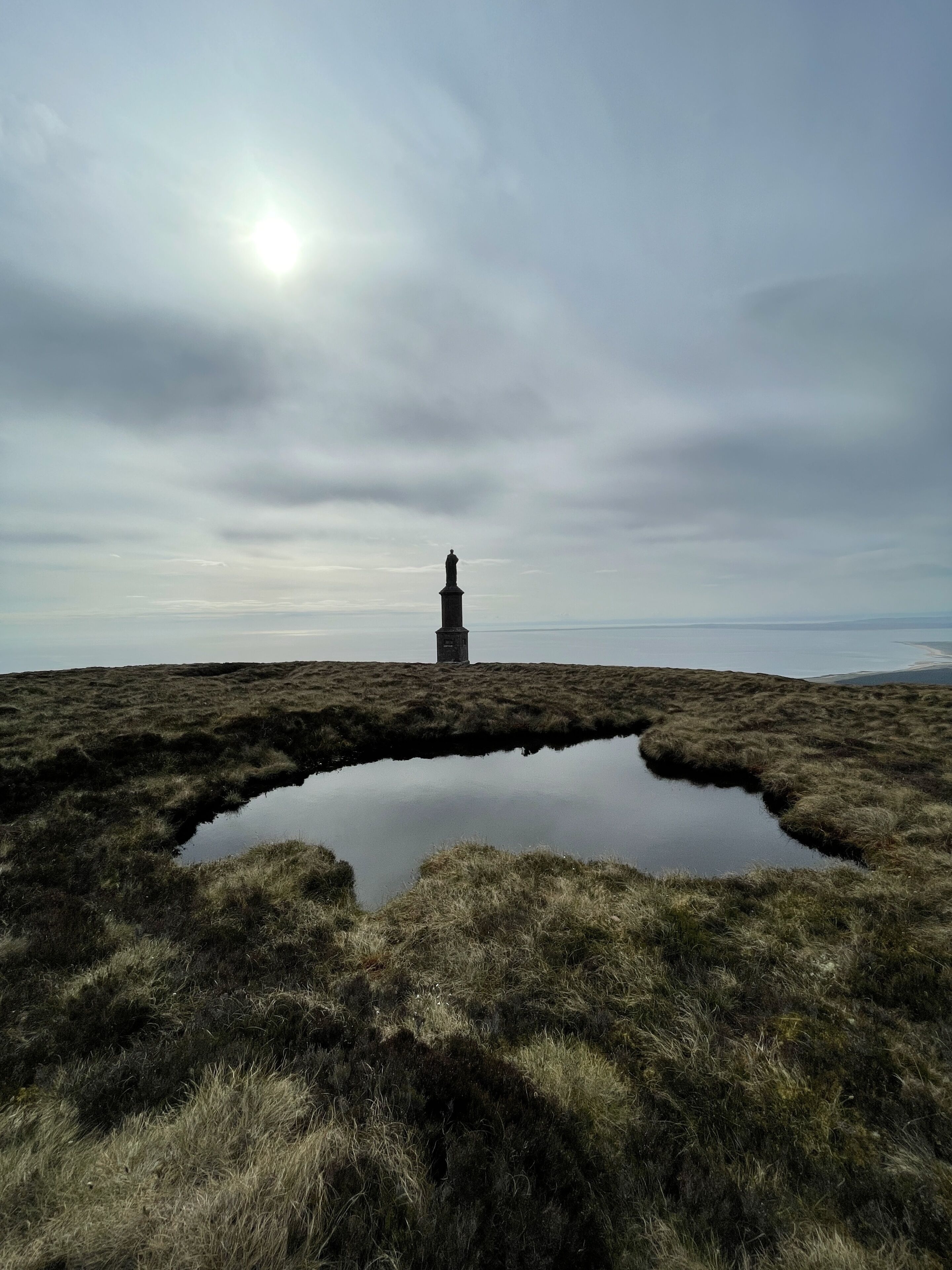 Un monumento solitario en una colina cubierta de hierba, con una masa de agua tranquila al frente.